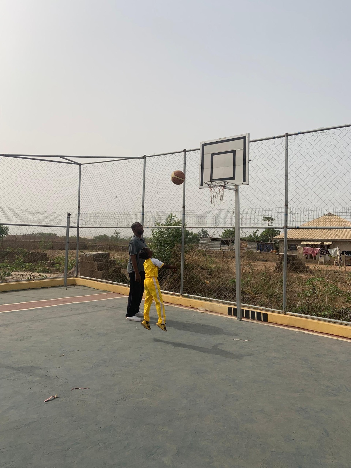 Young student leaping to shoot basketball with coach watching