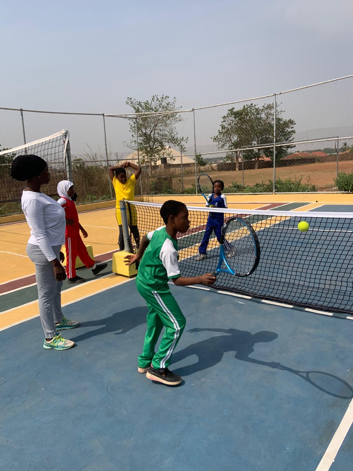 Pupil playing tennis with coach and teammates on sports court